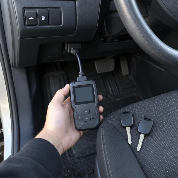 Two new transponder keys on the seat while a handheld programmer reads the car's diagnostic port.